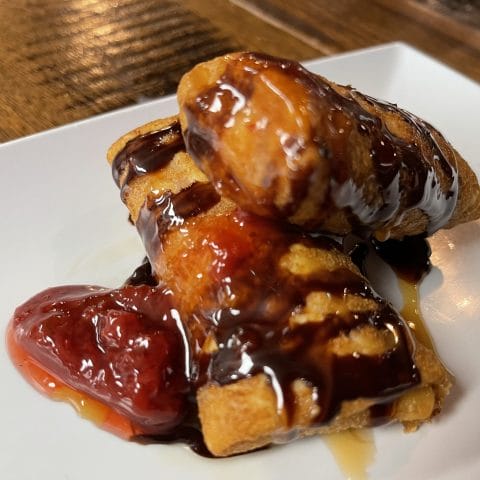 Decadent Raspberry Chimi from Atwater Street Tacos, combining raspberries and cream cheese in a fried tortilla, drizzled with chocolate syrup and caramel, garnished with fresh strawberries, presenting a fusion of classic Mexican flavors with a sweet twist.