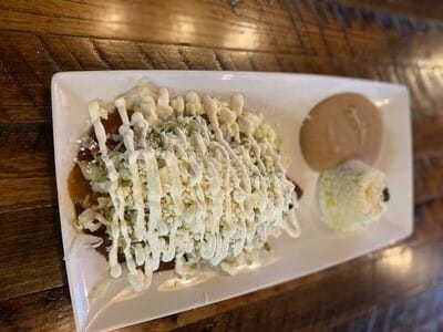 Plate of Cheese Enchiladas Rojo from Atwater Street Tacos - three white corn tortillas filled with melted shredded cheese, covered in tangy rojo sauce, served with rice, beans, lettuce, onion, queso fresco, and sour cream.