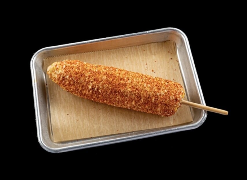 Image of Elote, a Mexican street food, featuring tender corn on the cob slathered in mayo, Cotija cheese, and tajin chili lime powder. A symphony of sweet, savory, tangy, and spicy flavors in one bite.